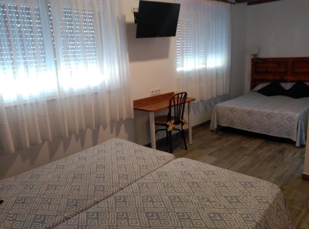 A room with two beds, a desk, a chair, a TV, and a window with curtains.