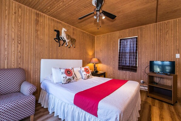 Una habitación con paneles de madera, una cama, un mueble para televisión y un ventilador de techo.