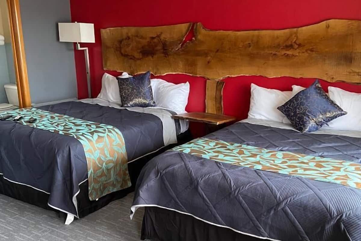 A hotel room with two beds, a red accent wall, and a wooden headboard.