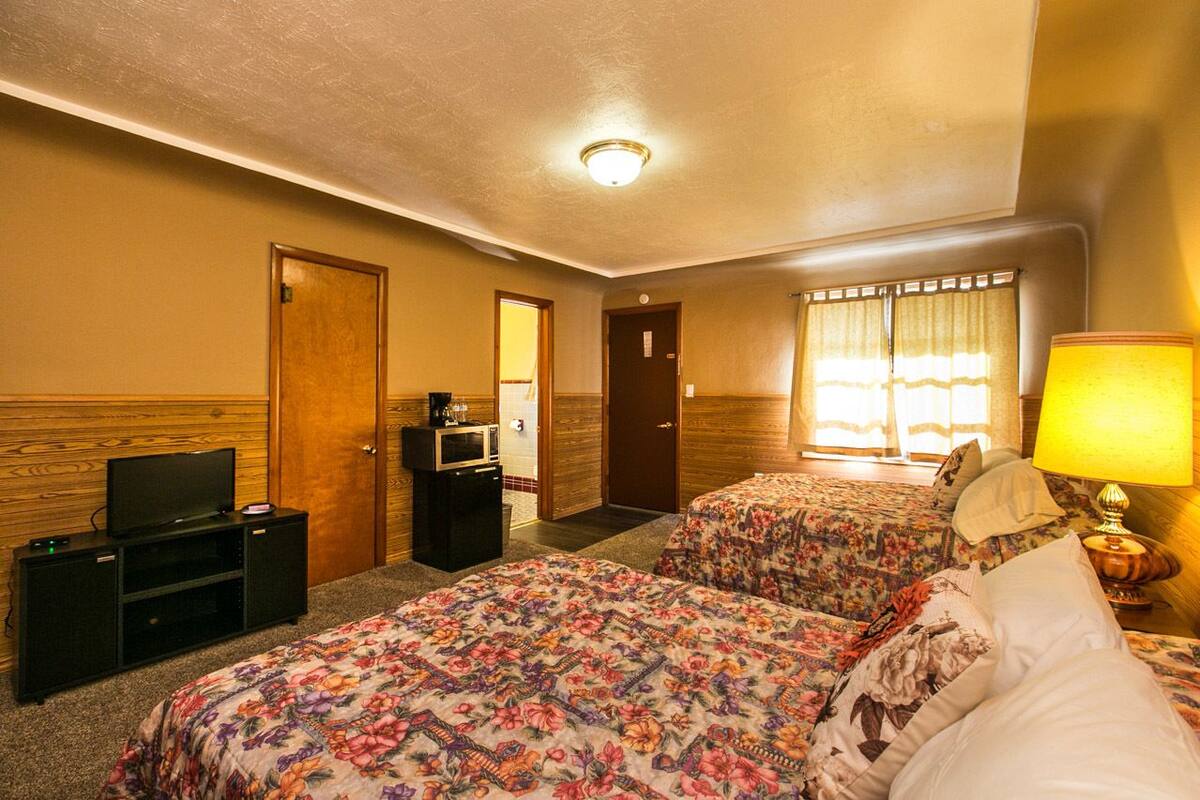 A hotel room with two beds, a television, a desk, and a window with curtains.