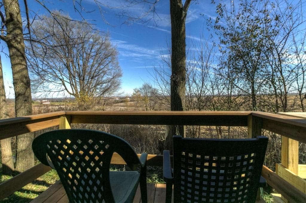 A wooden deck with two chairs and a table, overlooking a landscape with trees and a clear sky.