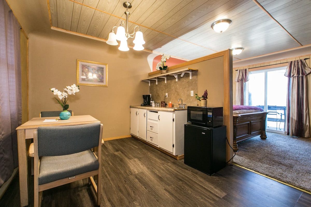 A compact room with a kitchenette, a dining area with a table and chairs, a bed, and a view of the outdoors.