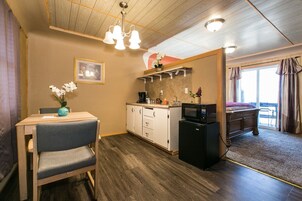 A compact room with a kitchenette, a dining area with a table and chairs, a bed, and a view of the outdoors.