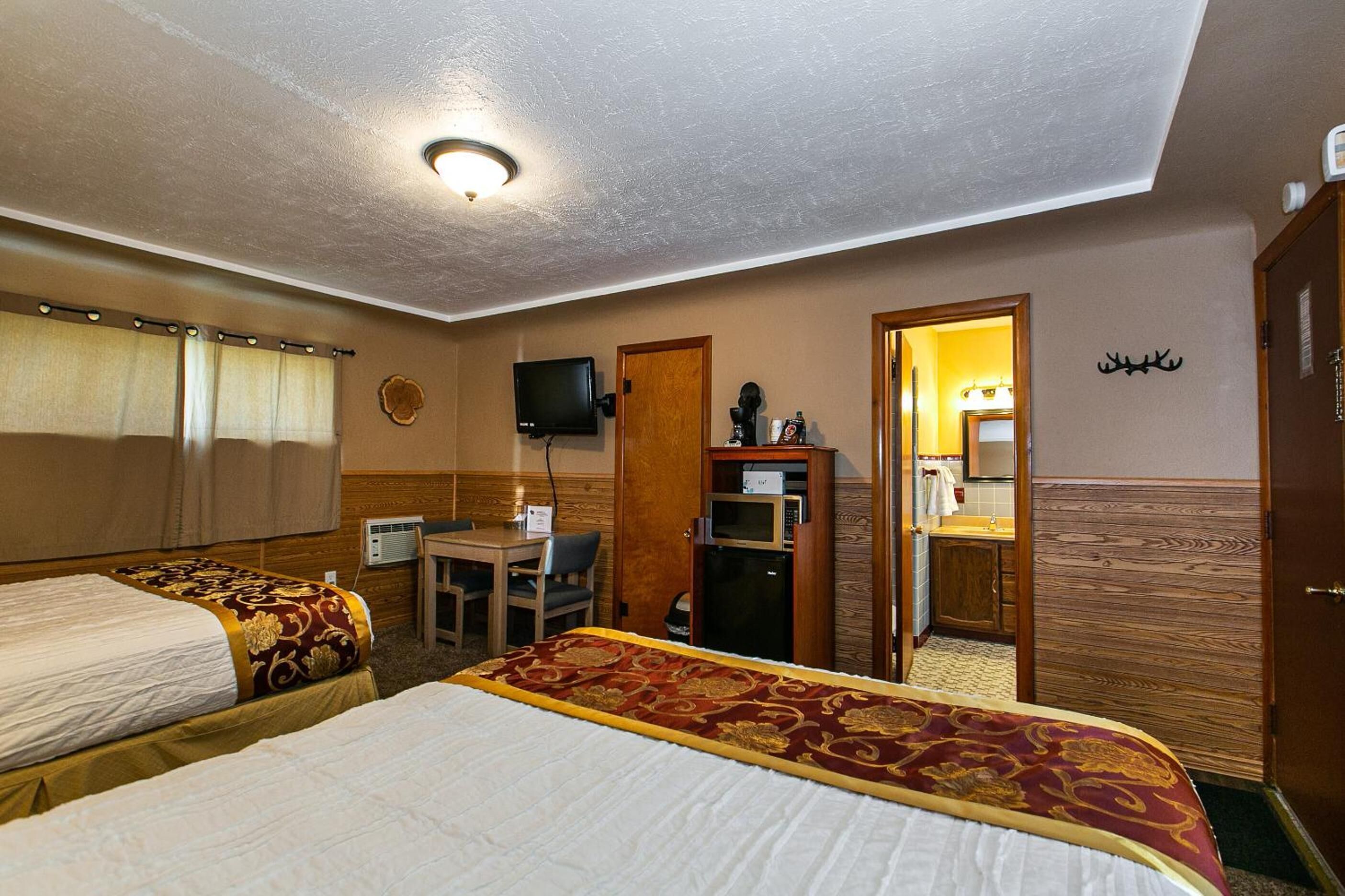 A hotel room with two beds, a desk, a television, a microwave, a bathroom, and a coat rack.