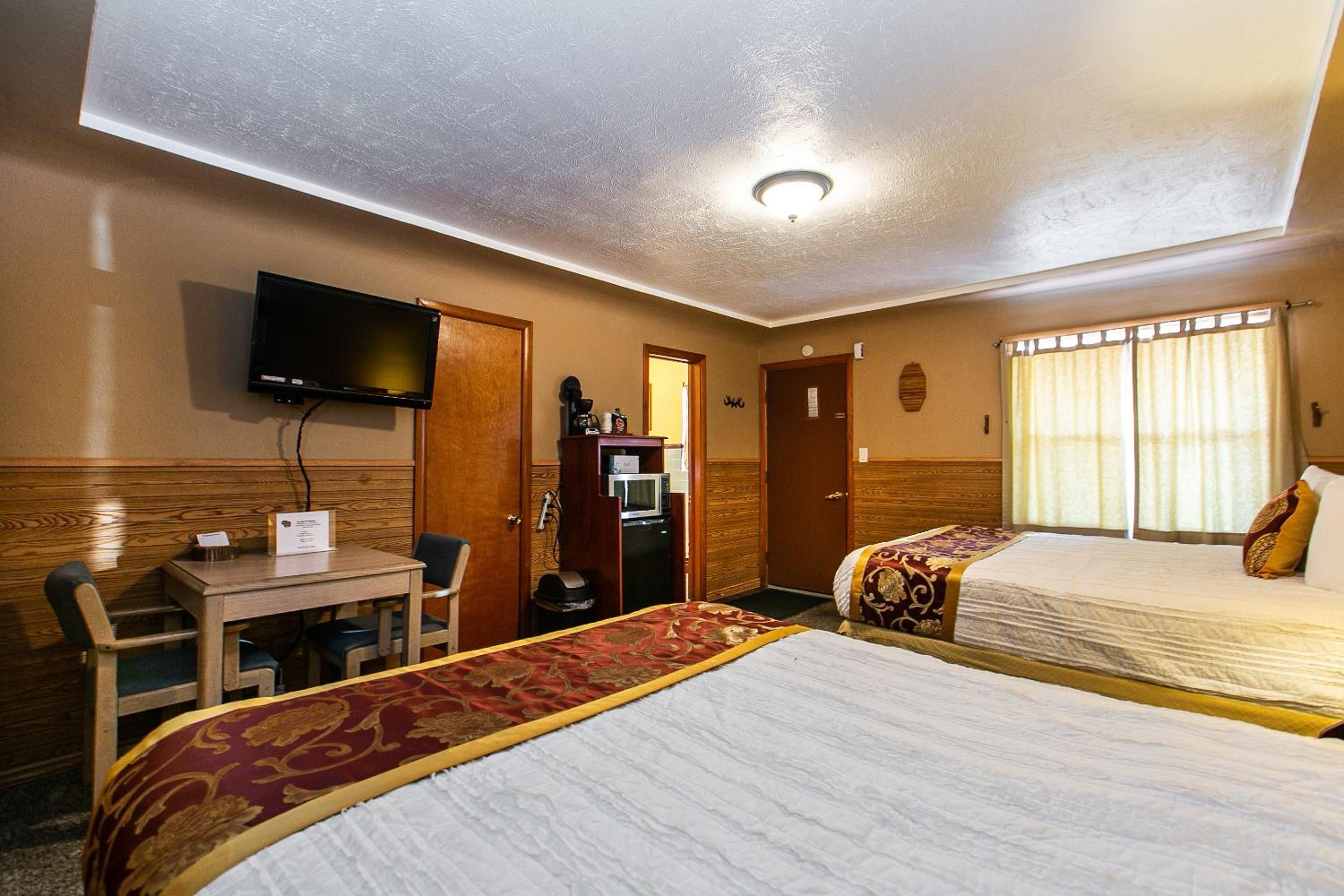 A hotel room with two beds, a desk, a television, and a kitchenette.
