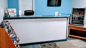 A reception area with a blue wall, a white door, a flat-screen TV, a vending machine, and a counter with a black chair. - Executive Inn Thomson (Thomson)