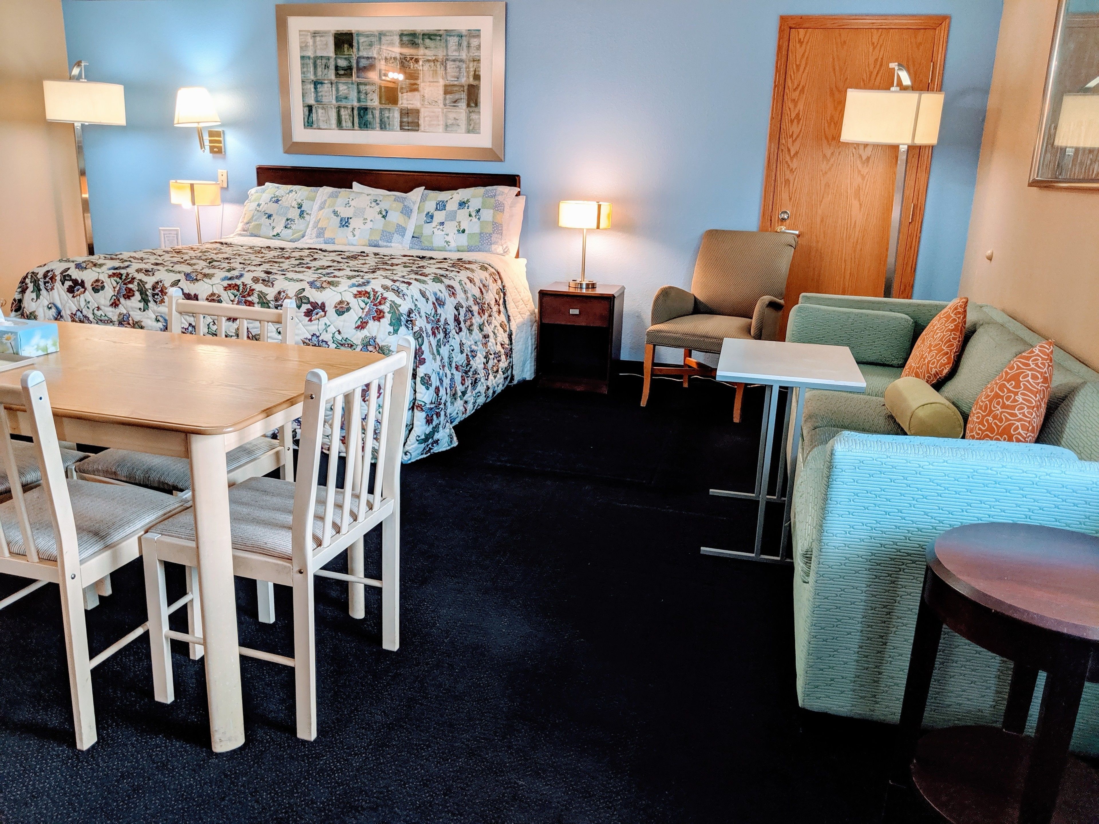 A hotel room with a bed, a desk, a chair, a sofa, and a small table.