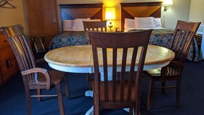 A hotel room with a round wooden table surrounded by four wooden chairs, a bed with patterned bedding, and a nightstand with a lamp. - Executive Inn Thomson (Thomson)