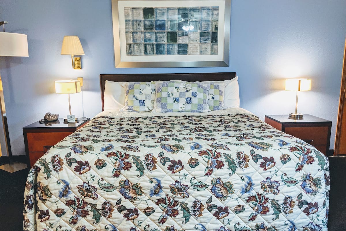 A neatly made bed with a floral quilt, two bedside lamps, a framed artwork above the bed, and a telephone on the nightstand.