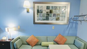 A room with a green sofa, two patterned pillows, a small table, a framed artwork, a lamp, and a telephone on a side table. - Executive Inn Thomson (Thomson)