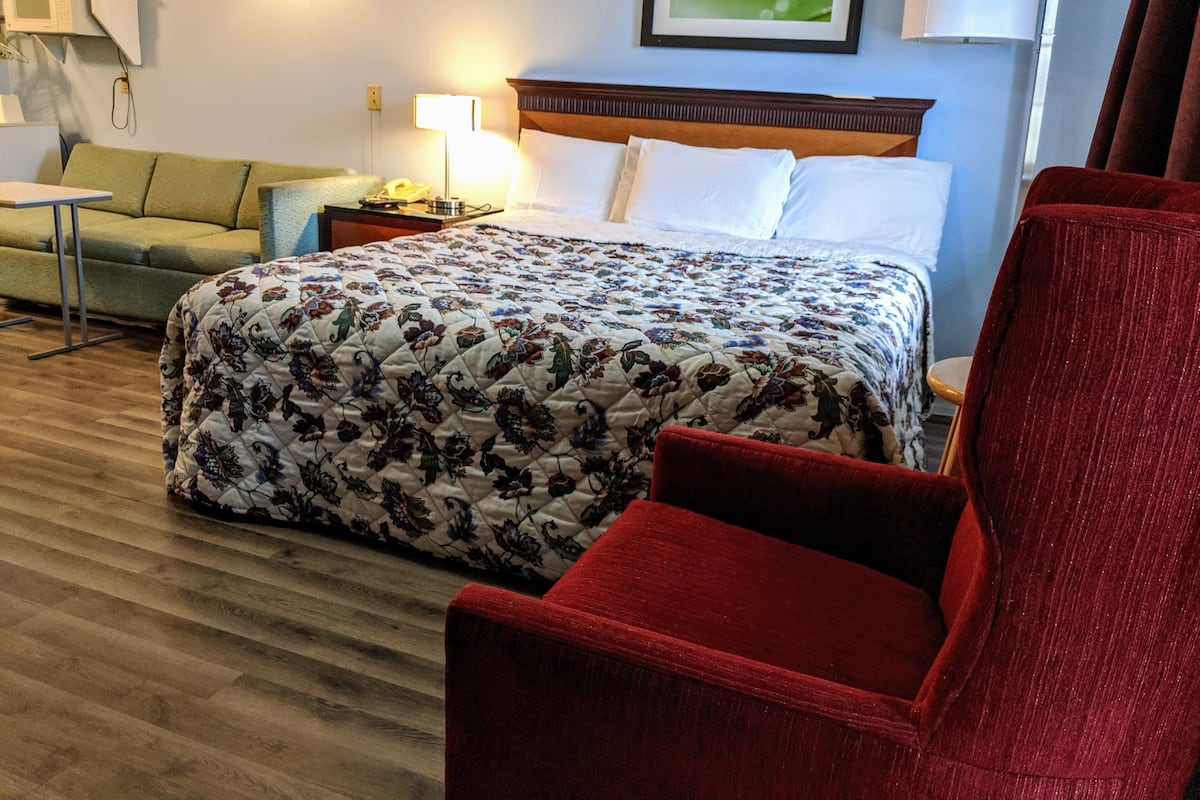 A hotel room with a large bed, a red chair, a small table, and a sofa.