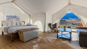 Ein Zeltraum mit Bett, Schreibtisch, Stuhl, einer Couch und Blick auf eine gebirgige Landschaft.