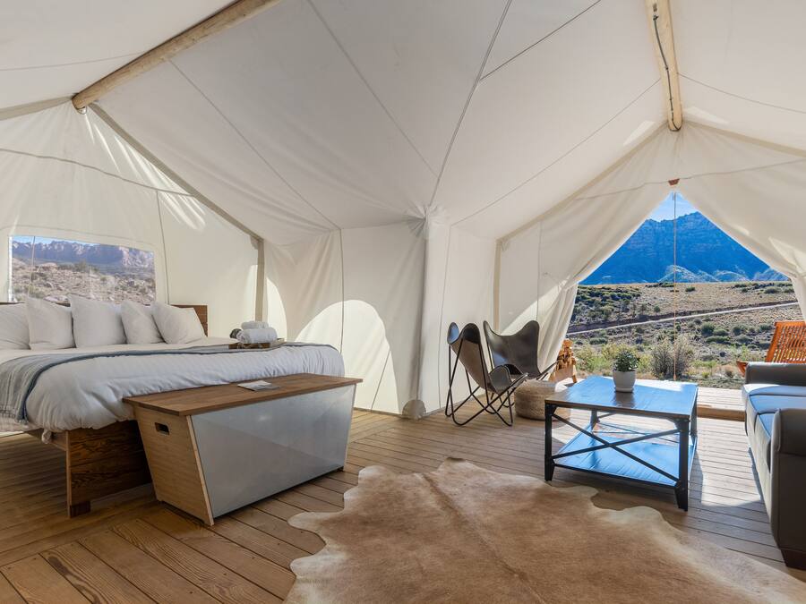 Une pièce aménagée comme une tente, avec un lit, un bureau, une chaise, un canapé et une vue sur un paysage montagneux.