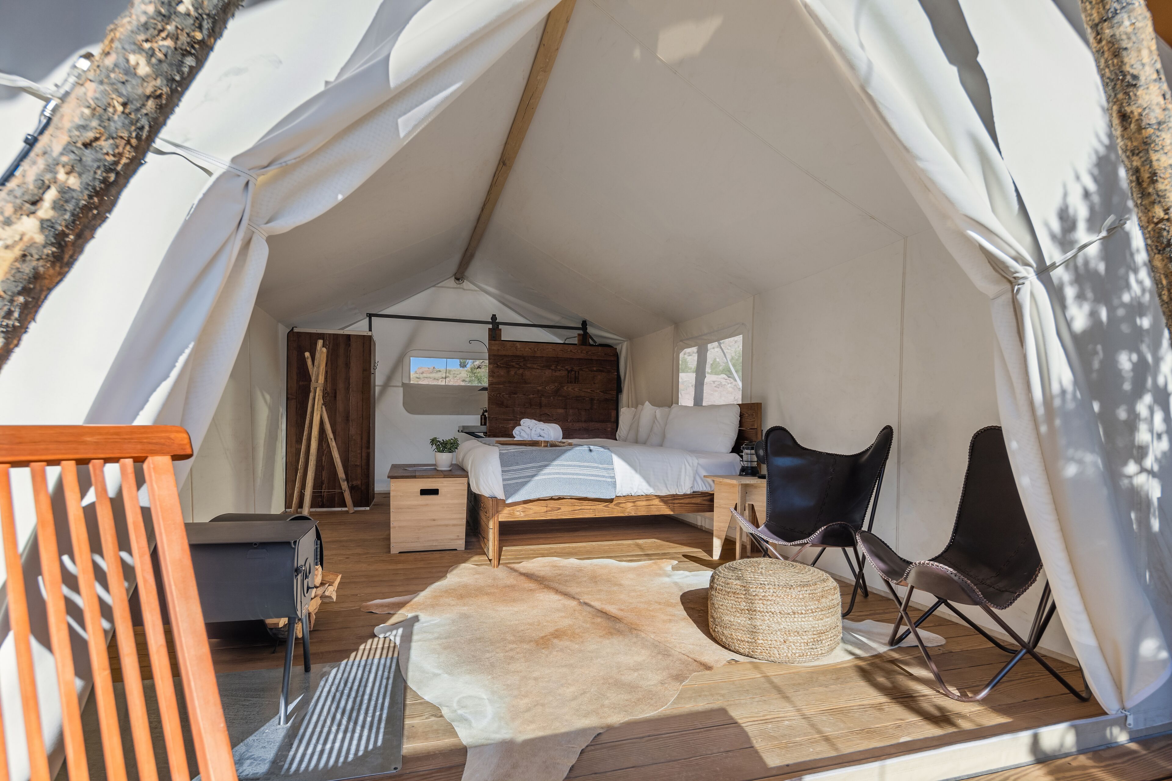 A tented accommodation with a bed, wooden flooring, a small table, and a chair.
