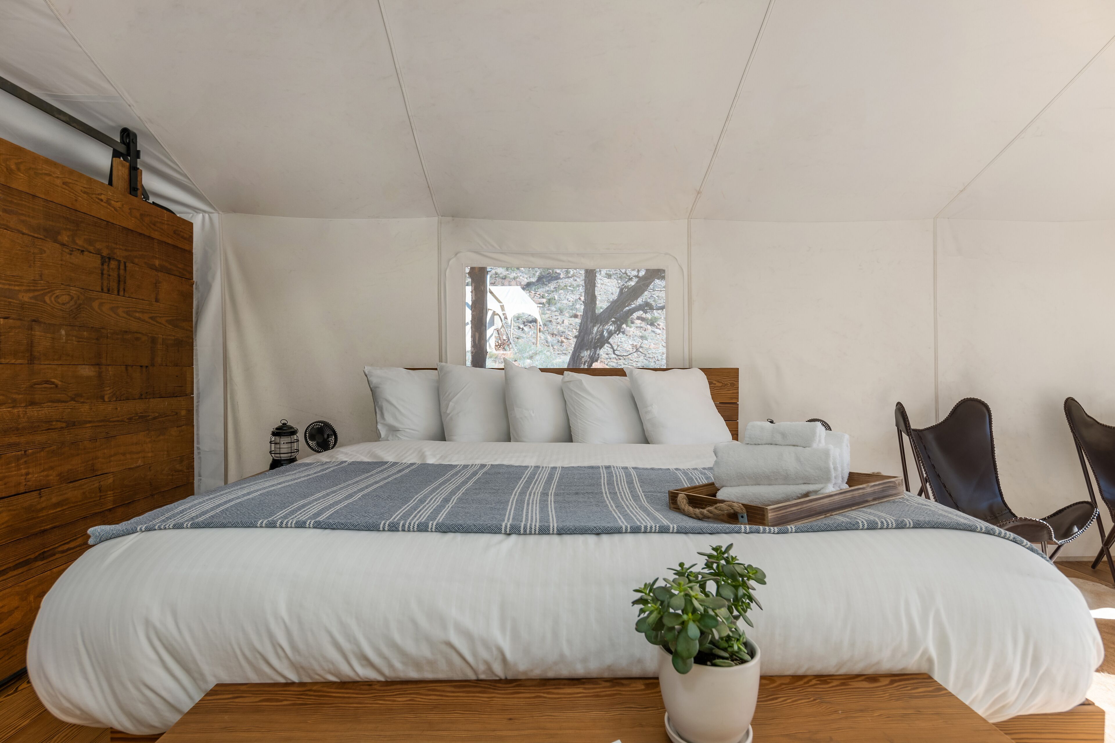 A bedroom with a large bed, a wooden wardrobe, a window with a view of trees, and two chairs.