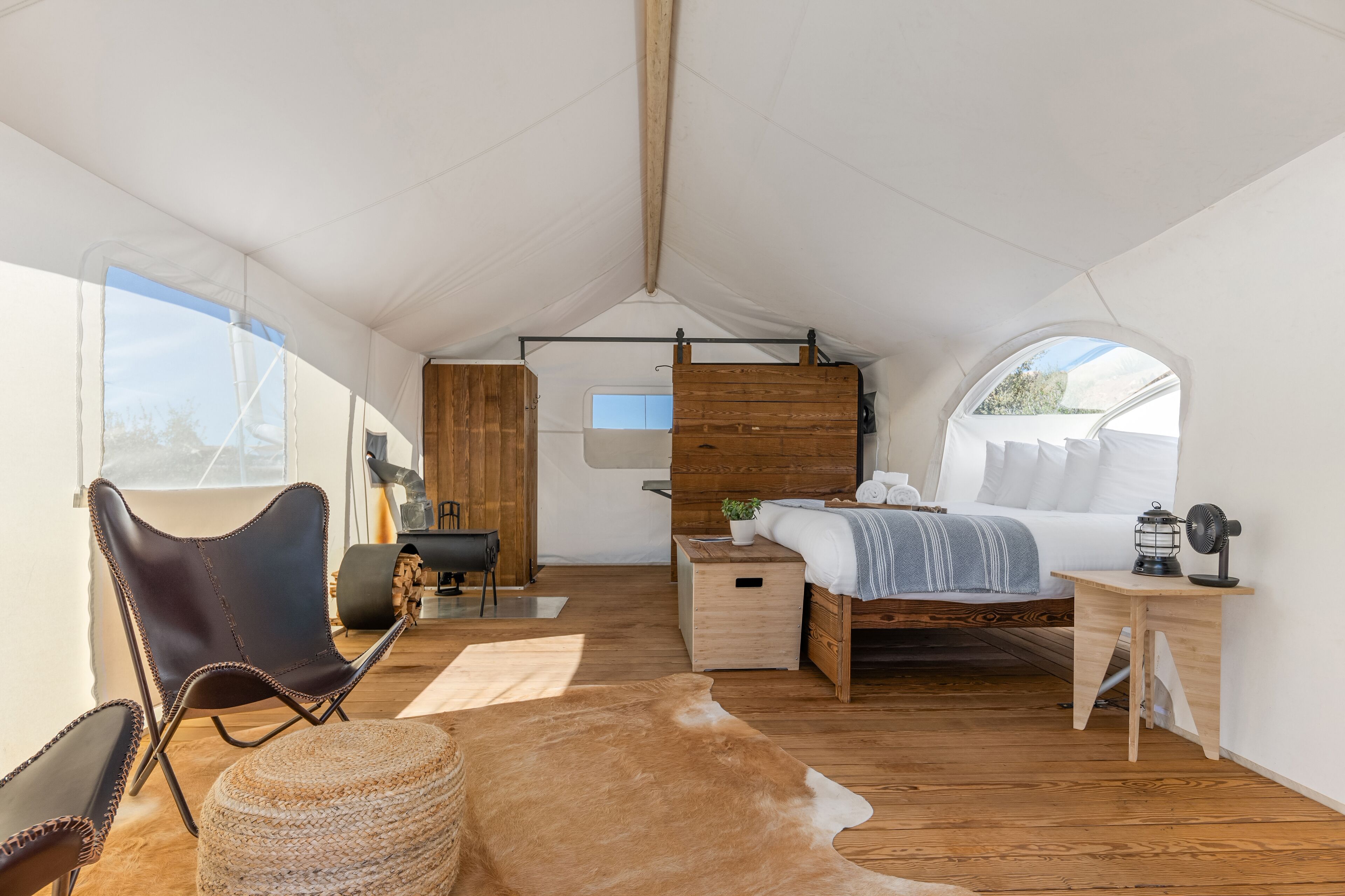 Una habitación con carpa, cama, suelo de madera, una silla, una mesita y una ventana.