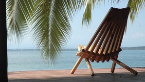 Un fauteuil de relaxation en bois sur une terrasse en bois, avec vue sur la mer et les palmiers.