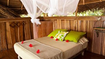 Ein hölzernes Bett mit Baldachin, mit grünen und beigen Kissen und roten Blumen auf der Tagesdecke.
