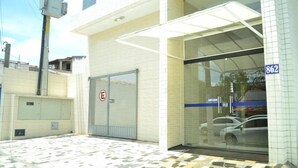 A building with a closed metal shutter door, a glass entrance with a blue stripe, and a number '862' on the wall. - Prime Hotel (Feira de Santana)