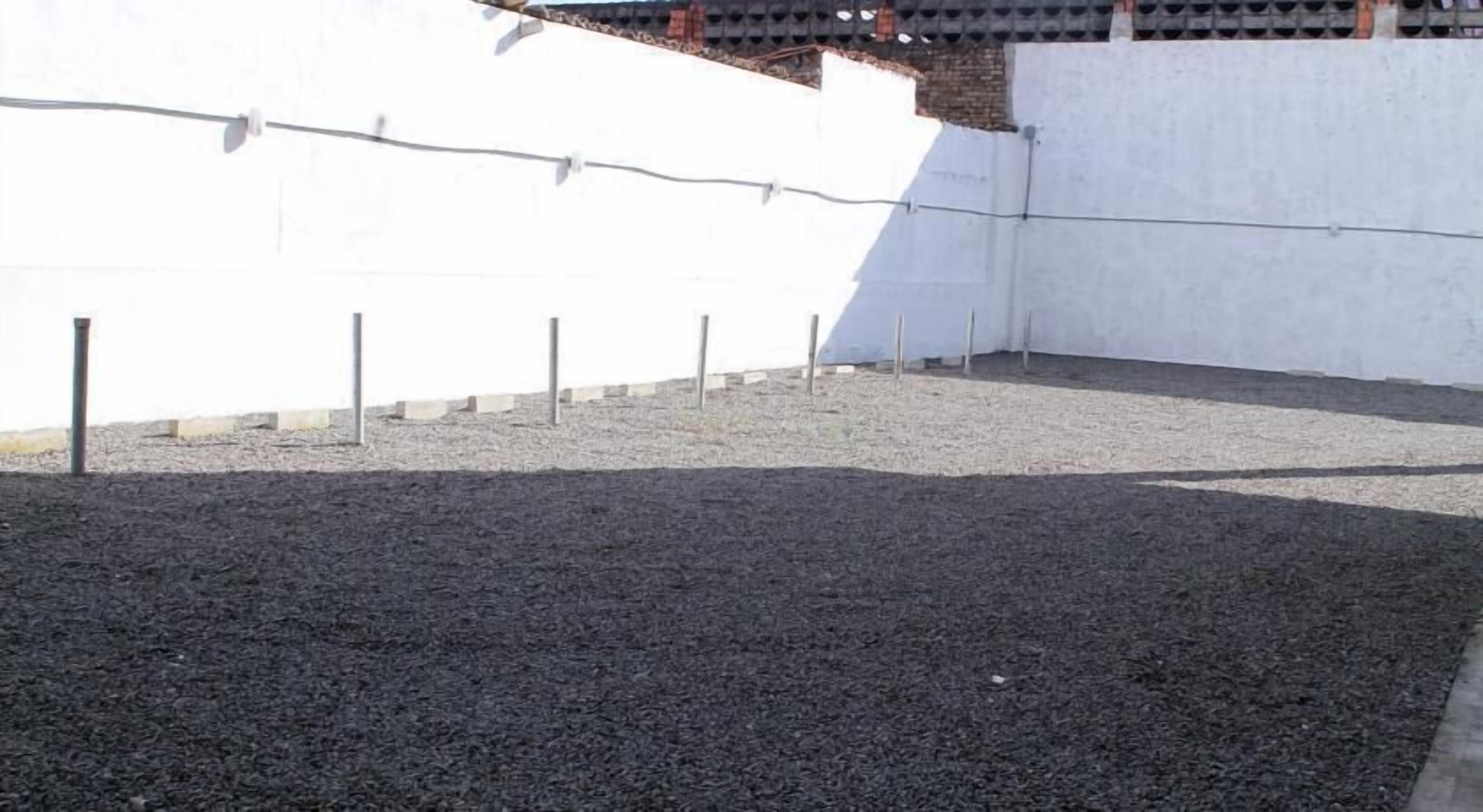 An outdoor area with a gravel surface, white walls, and a metal fence.