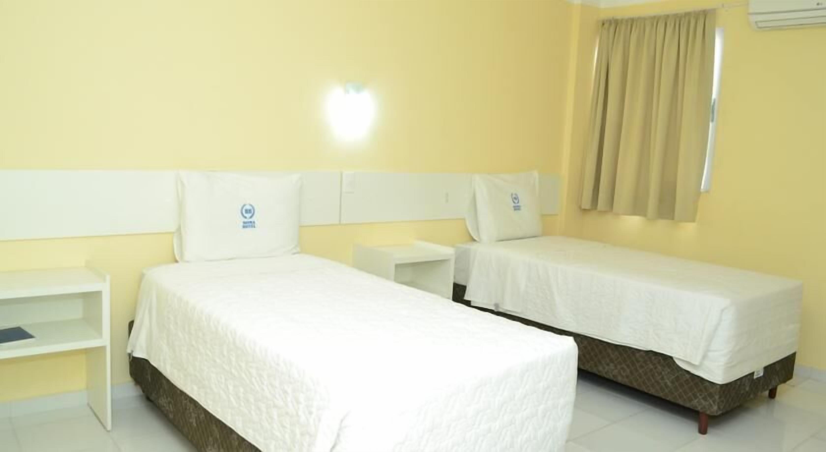 Een hotelkamer met twee eenpersoonsbedden, een nachtkastje en een raam met gordijnen.