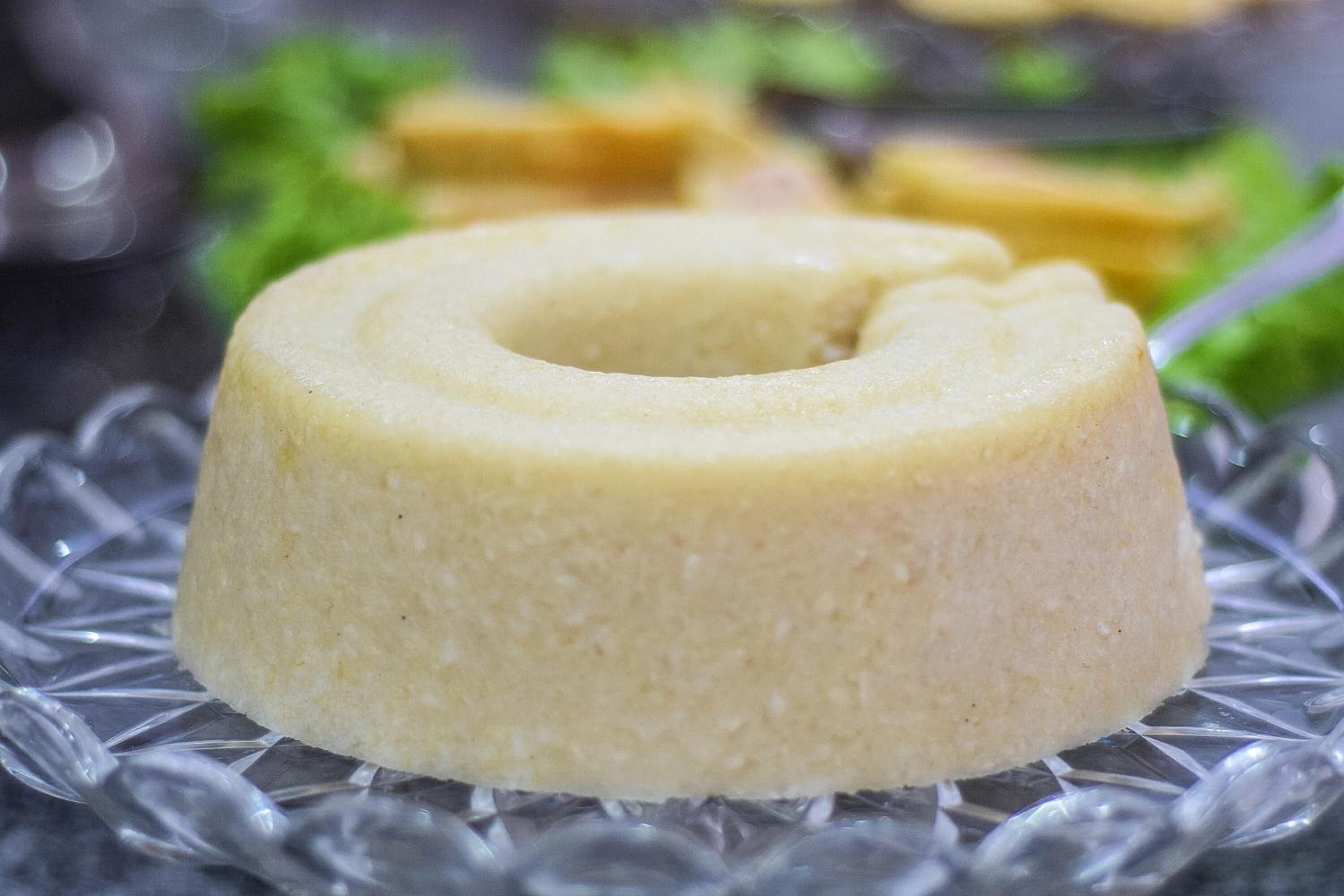 Ein einzelnes, rundes, blassgelbes Dessert auf einer Glasplatte.