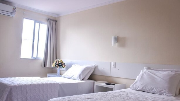 A hotel room with two beds, a nightstand, a wall-mounted light, and a window with curtains. - Prime Hotel (Feira de Santana)