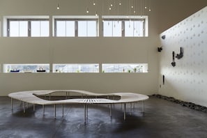 A spacious interior with large windows, a unique curved bench, and a patterned wall. - AQUA x IGNIS (Komono)