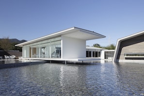 A modern building with a glass facade, a pool area, and a clear sky. - AQUA x IGNIS (Komono)