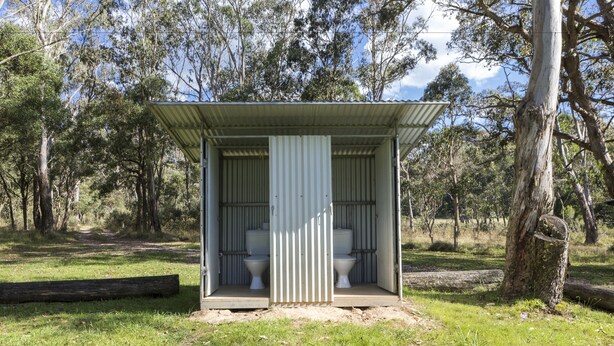 A portable toilet facility with two toilets, surrounded by a grassy area and trees. - Little Styx Cabins (Ebor)