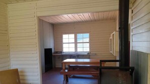 A room with wooden walls, a window, a table, a chair, and a fireplace. - Little Styx Cabins (Ebor)