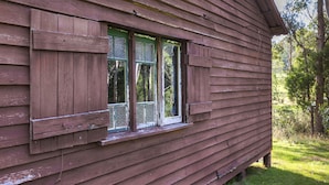 A rustic wooden cabin with a window featuring a green frame and a wooden shutter. - Little Styx Cabins (Ebor)