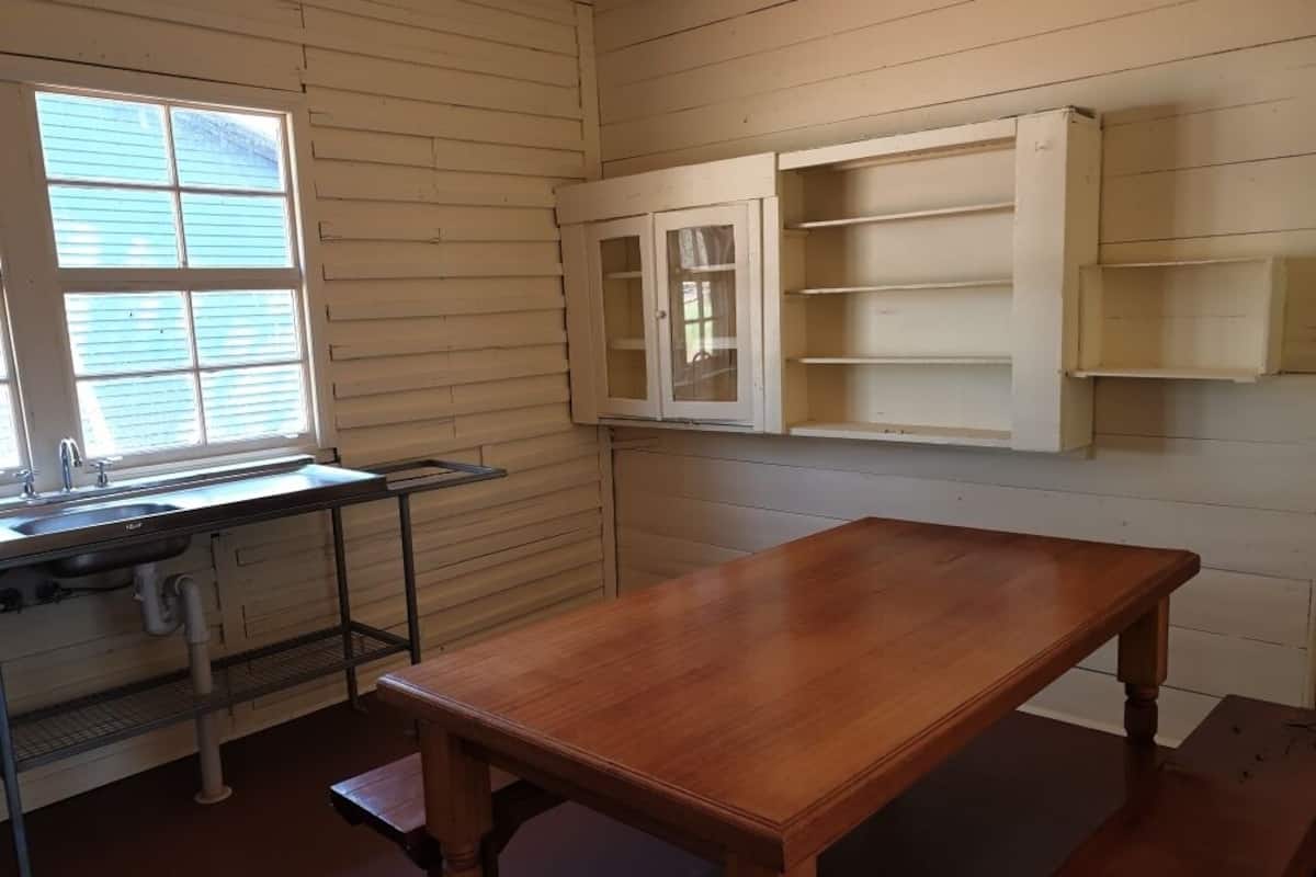 A room with a wooden table, a window with blinds, a sink, and built-in shelves.
