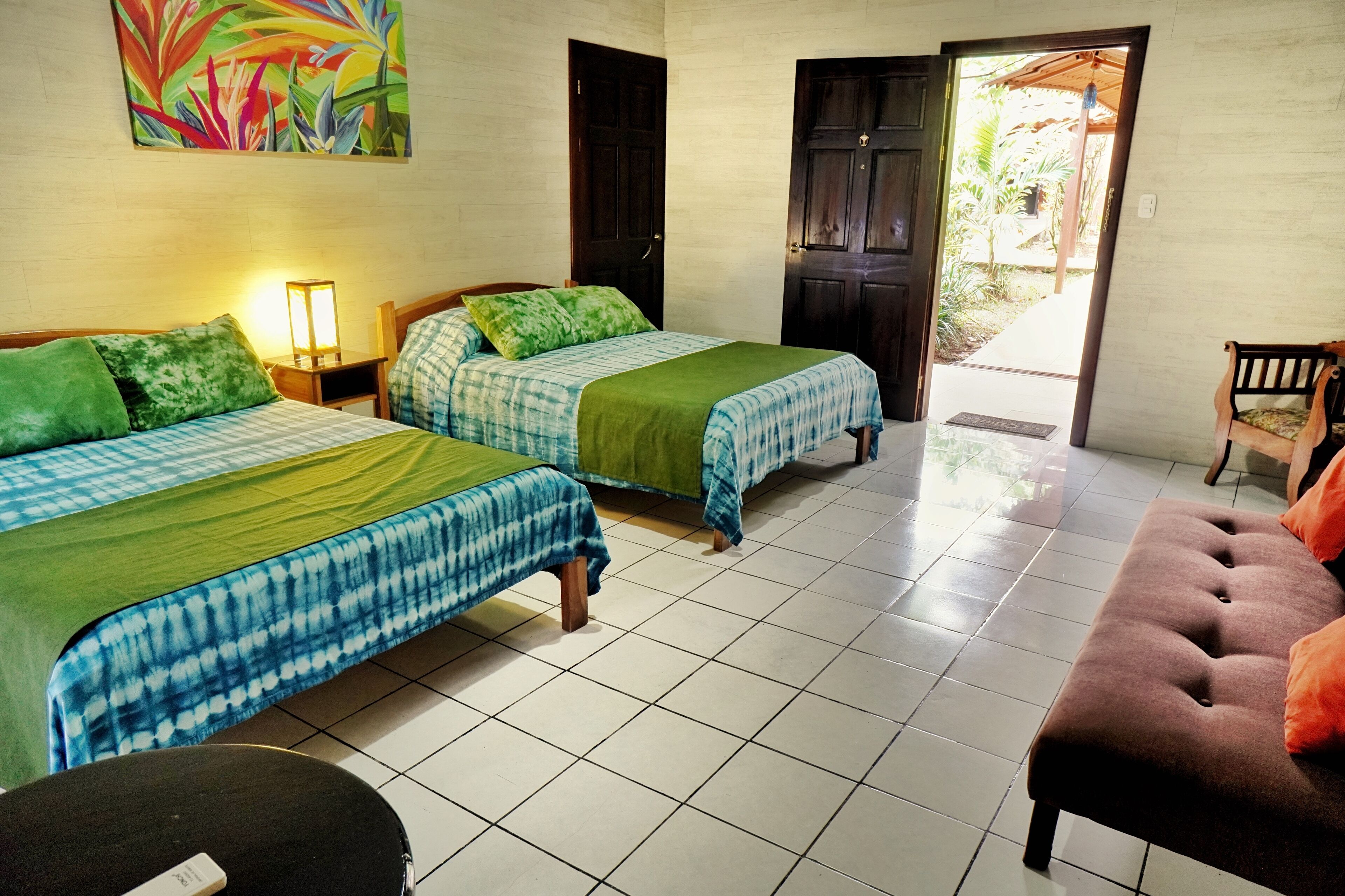 Habitación de hotel con dos camas, un sofá, una mesita de noche y una puerta que da a un balcón.