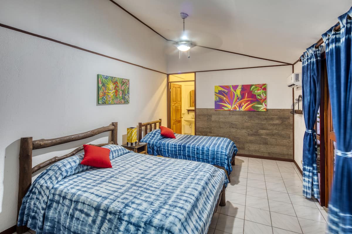 A room with two beds, a wooden headboard, a ceiling fan, and artwork on the walls.