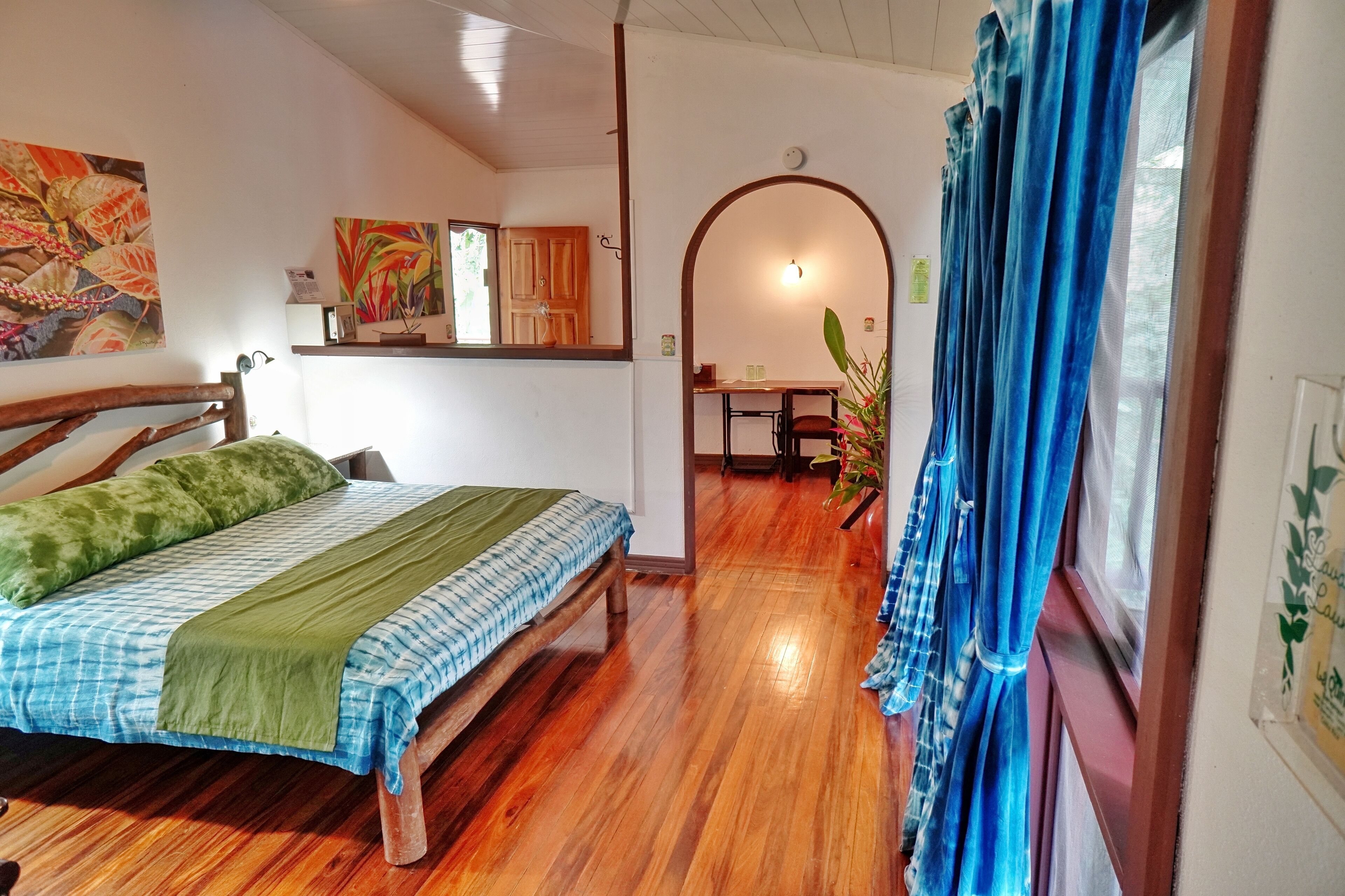 A room with a wooden bed, a desk, and a chair, with a window covered by blue curtains.