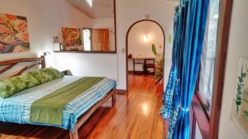 A room with a wooden bed, a desk, and a chair, with a window covered by blue curtains.