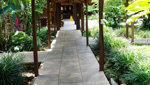 Uma galeria coberta com chão de azulejos, rodeada por vegetação exuberante e plantas.