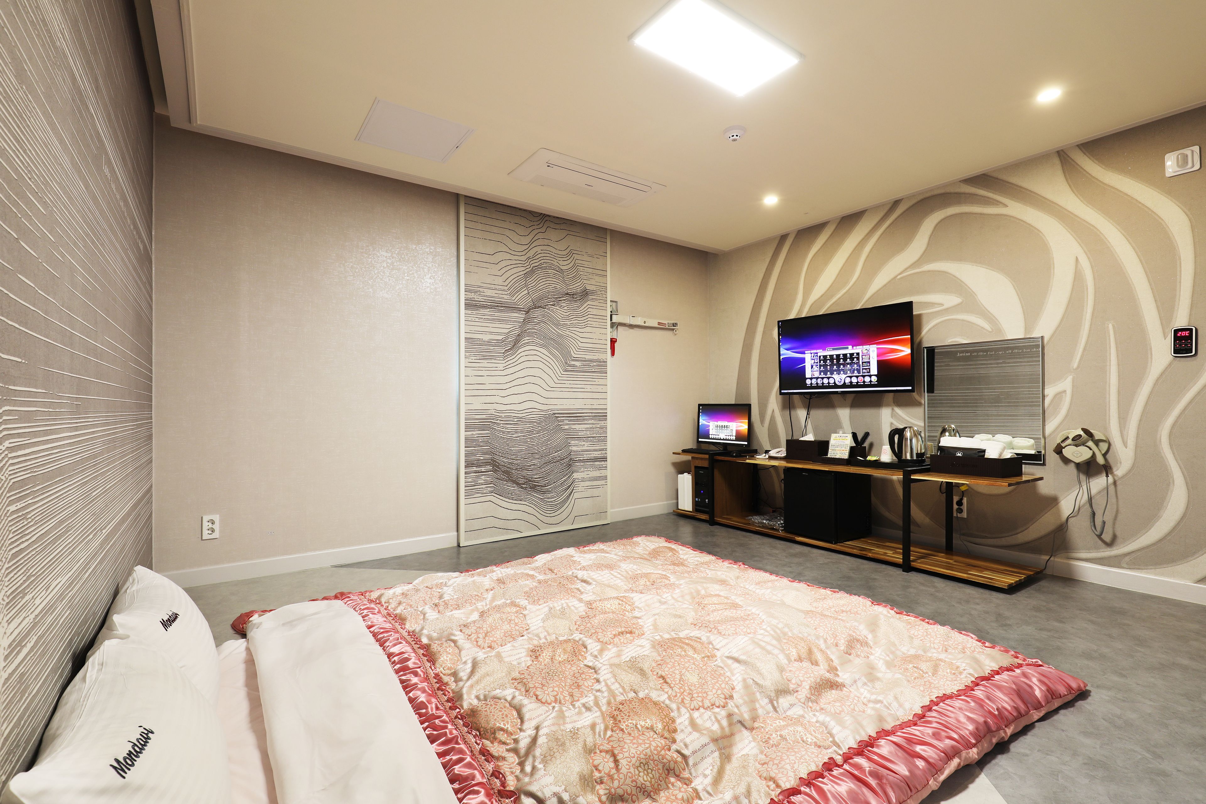 A hotel room with a large bed, a TV, a desk with a computer, and a wall with a unique design.