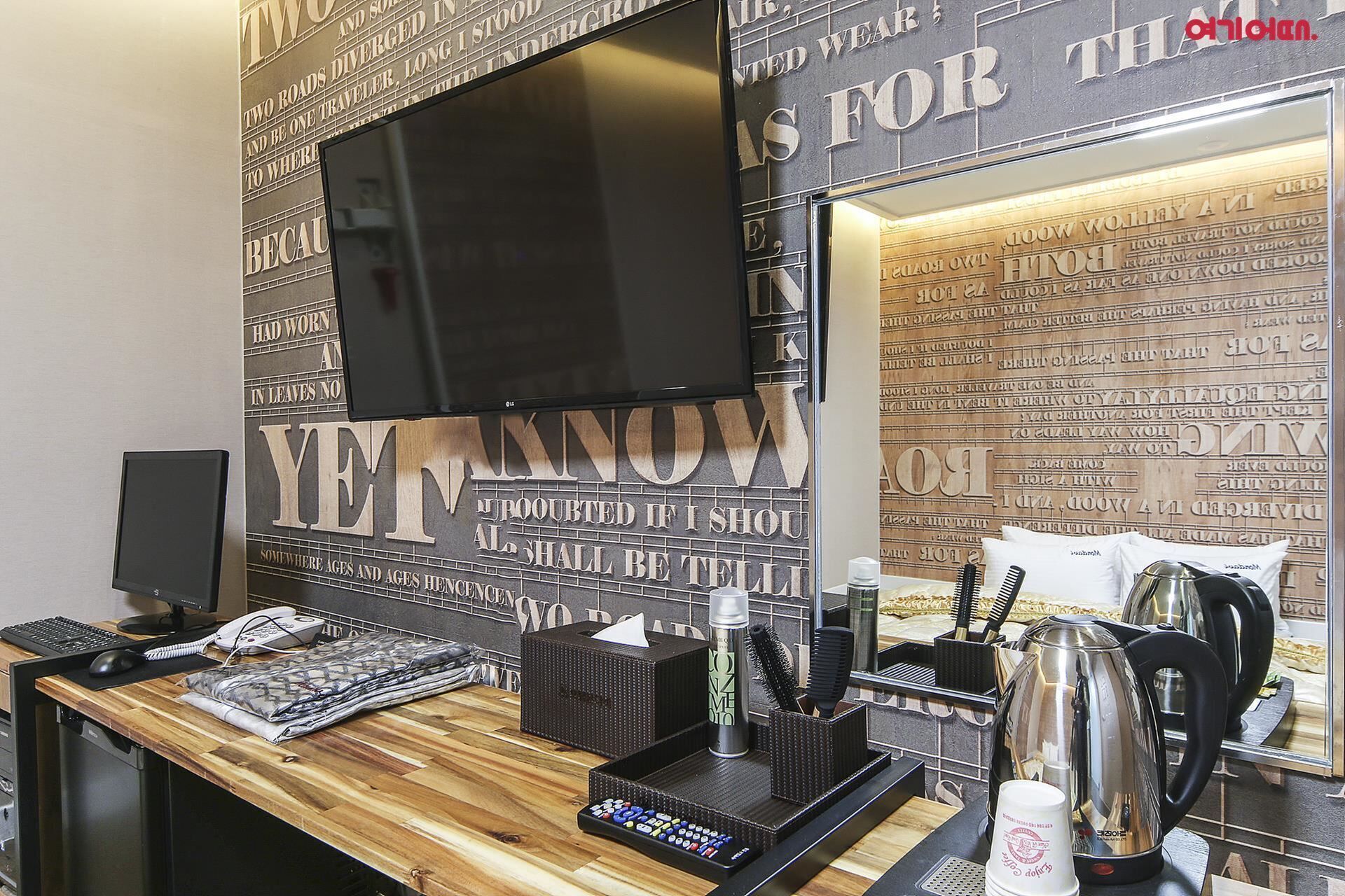 Habitación de hotel con un escritorio de madera, un televisor de pantalla plana montado en la pared y un espejo que refleja la decoración.