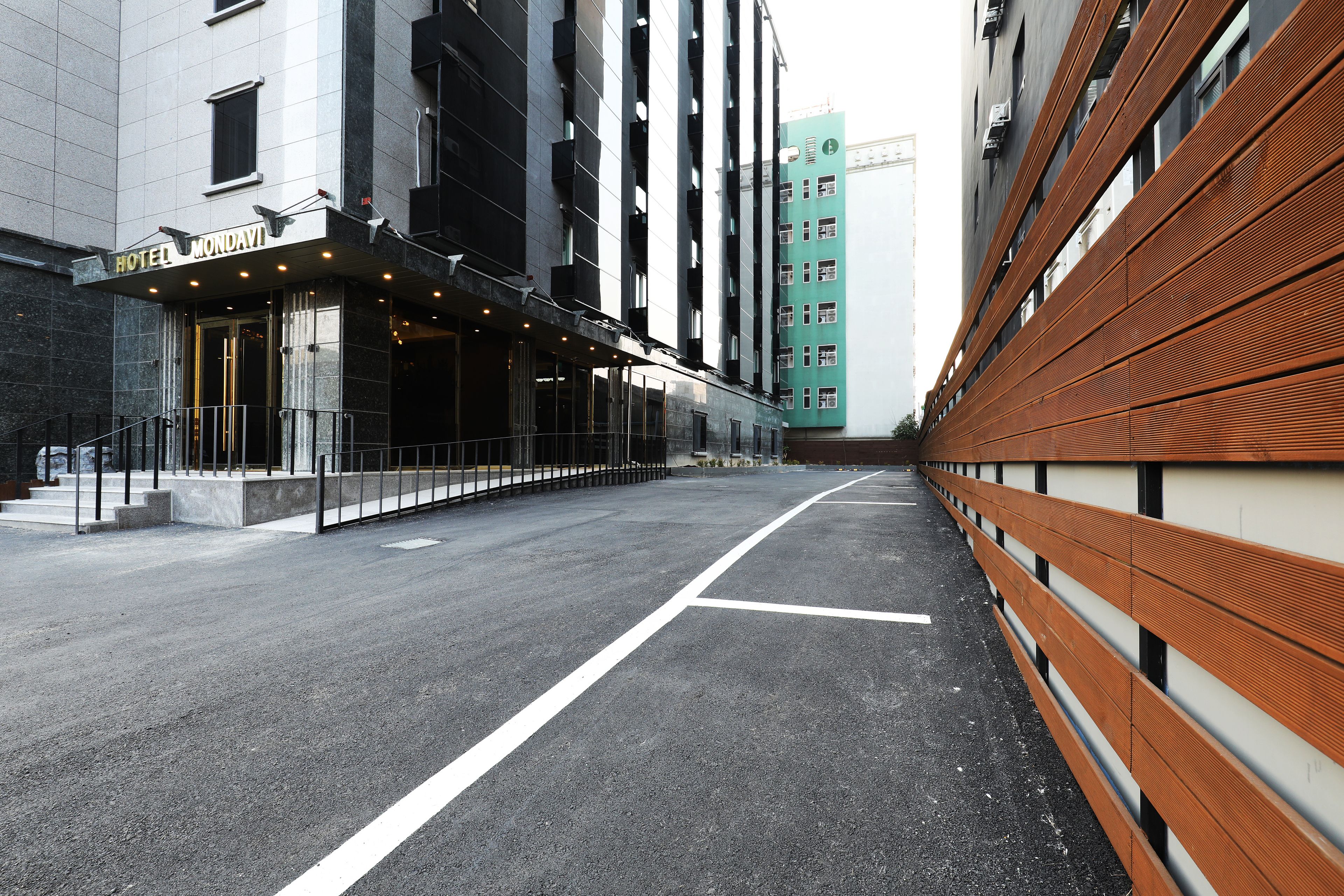 A modern hotel entrance with a clear pathway leading to the entrance, a well-maintained pavement, and a wooden bench along the side.