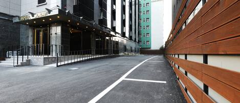 A modern hotel entrance with a clear pathway leading to the entrance, a well-maintained pavement, and a wooden bench along the side.