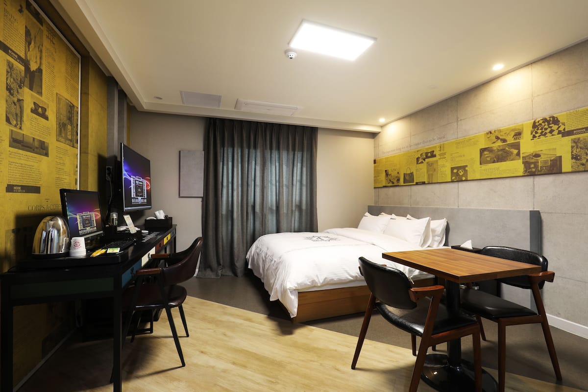 A hotel room with a bed, desk, chairs, and a television.