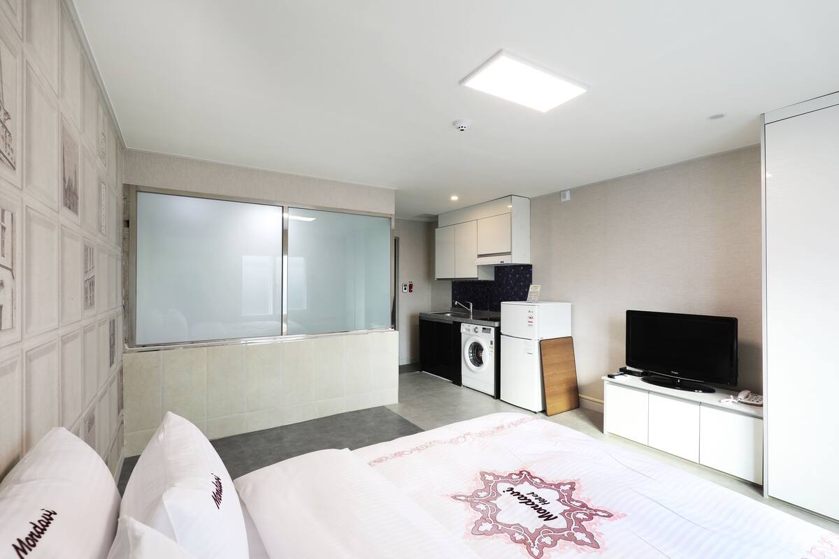 A hotel room with a bed, a television, a washing machine, and a kitchenette.