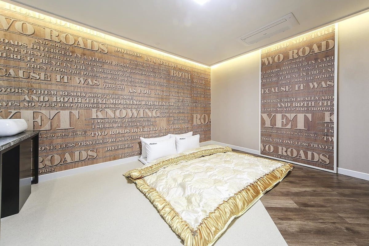 A bedroom with a large bed, a bedside table, and a wall with a repeating pattern of text.