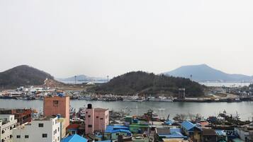 Un pueblo costero con un puerto deportivo, edificios con techos azules y un paisaje montañoso al fondo.