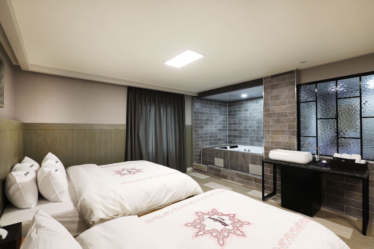 A hotel room with two beds, a bathroom with a bathtub, and a large window with a view.