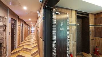 A hotel corridor with wooden paneling, a herringbone floor pattern, and a fire extinguisher near the elevator.