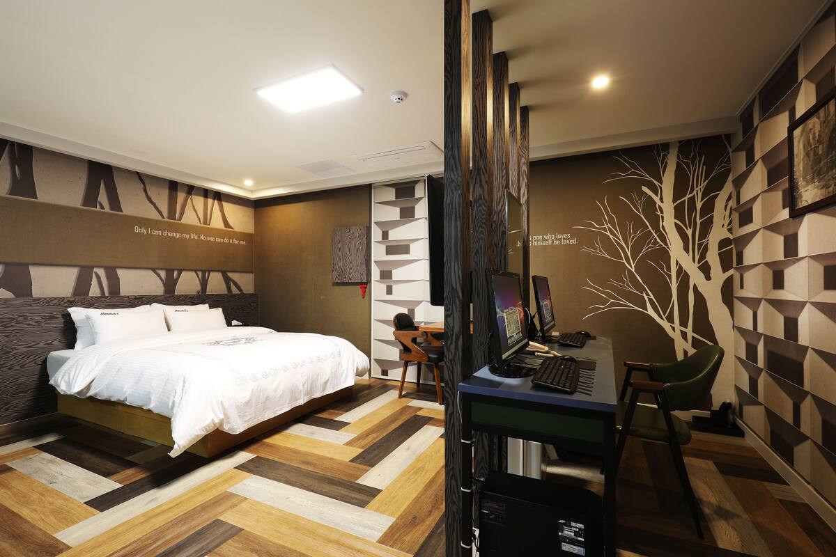 A modern hotel room with a large bed, a desk with a computer, and a chair.