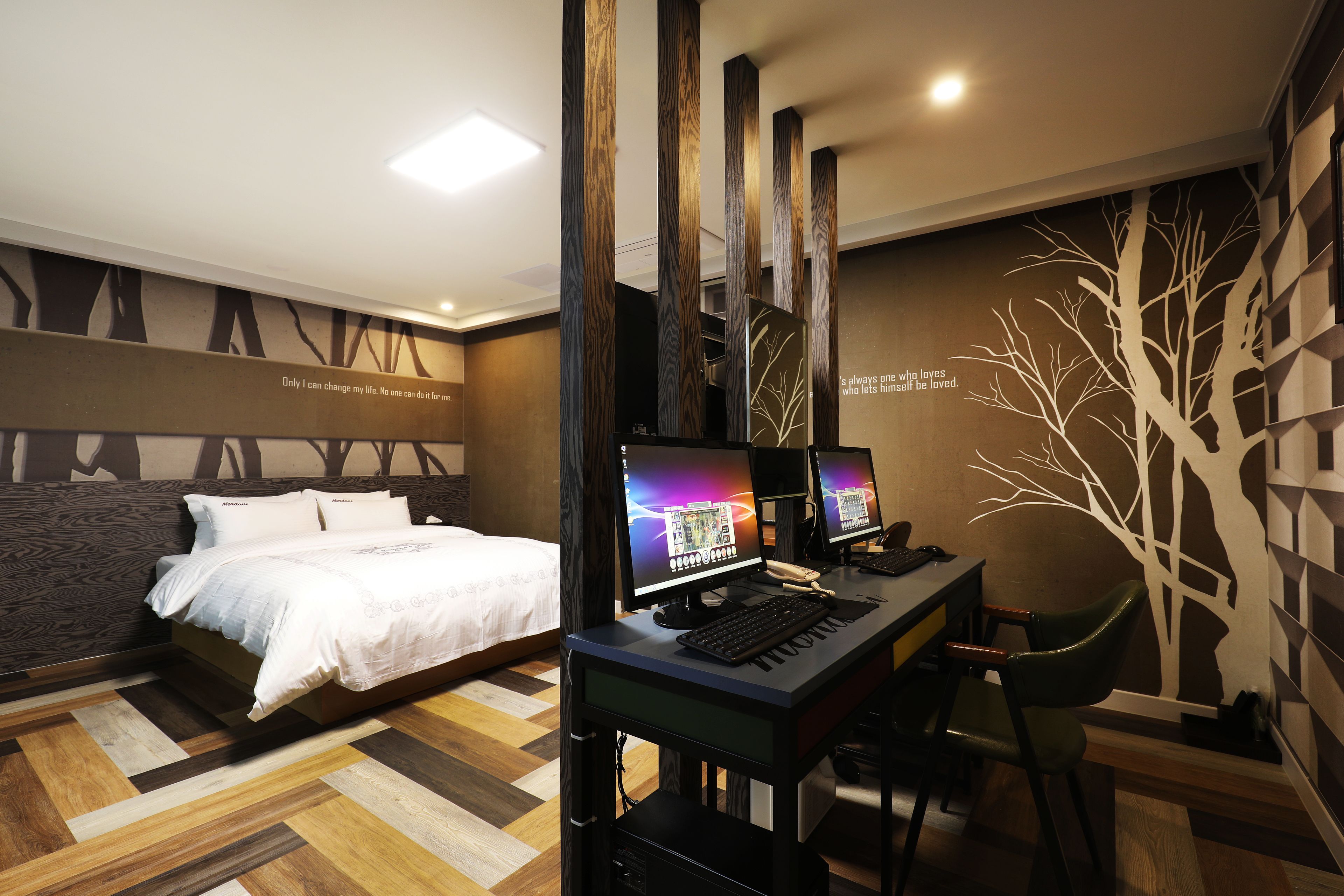 A modern hotel room with a bed, two computer desks, and a chair.